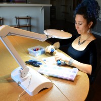 rebeca mojica sitting at table making chainmaille using table craft lamp by brightech