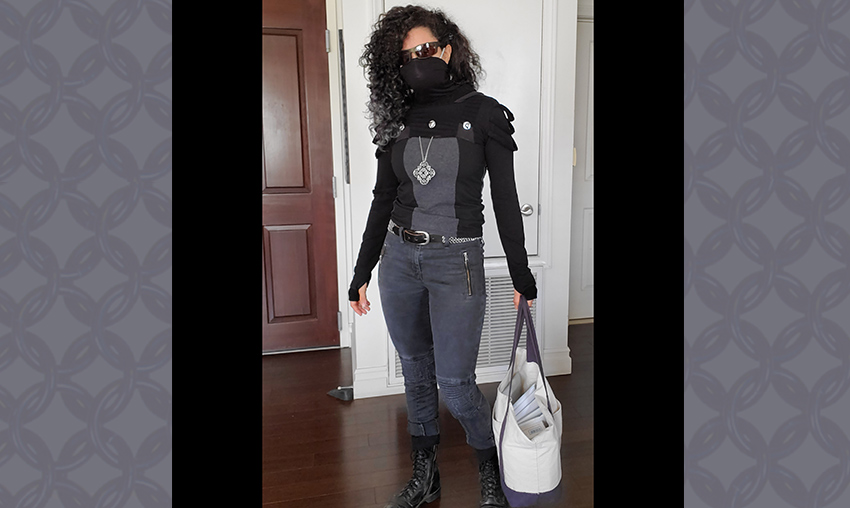 Rebeca wearing dystopian clothing with a black face mask and holding a bag of packages