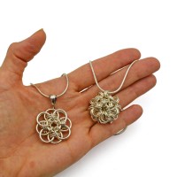 a palm holding two sterling silver chainmaille pendants