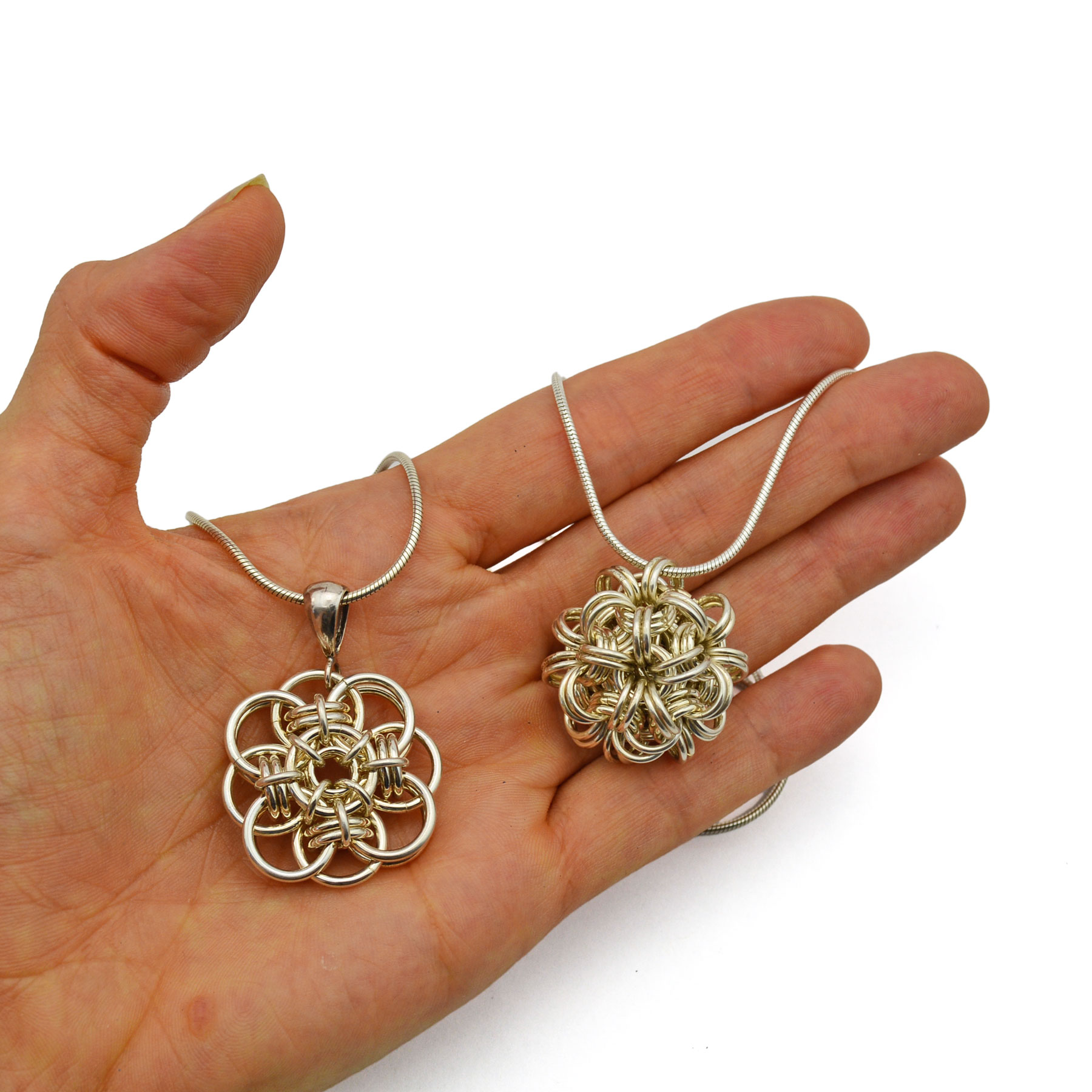 a palm holding two sterling silver chainmaille pendants 